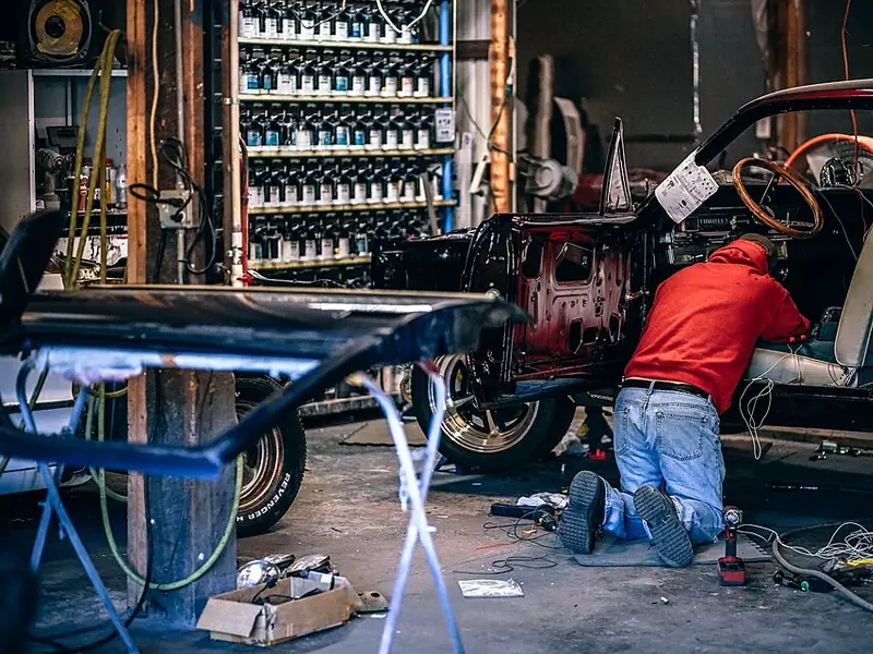 Mechanic kneeling inside a stripped classic car during restoration